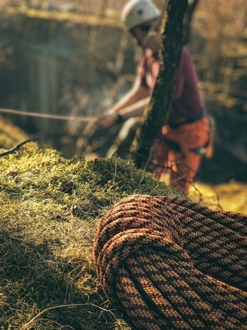 A climber part-way up a knotted rope on an outdoor timber climbing frame.