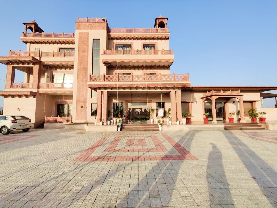 The hotel's front elevation from the paved forecourt: three storeys of carved sandstone columns, latticed balcony railings and a covered entrance porch, above paving laid in a red and grey geometric pattern.