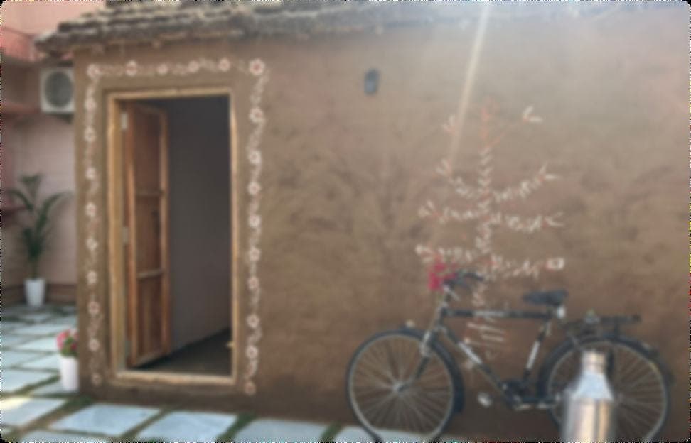 A mud-plastered village house under a tiled roof, white mandana folk painting framing the open doorway and climbing the wall in a tree motif, with an old black bicycle and a steel milk churn propped beside it.