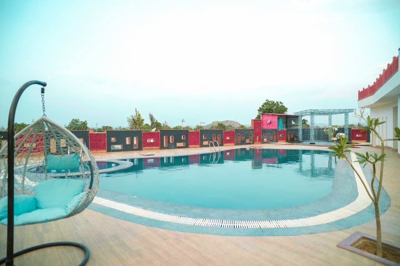 The infinity pool curving away toward open country, a hanging rattan egg chair in the foreground and a run of pink and charcoal cabana screens along the far edge.